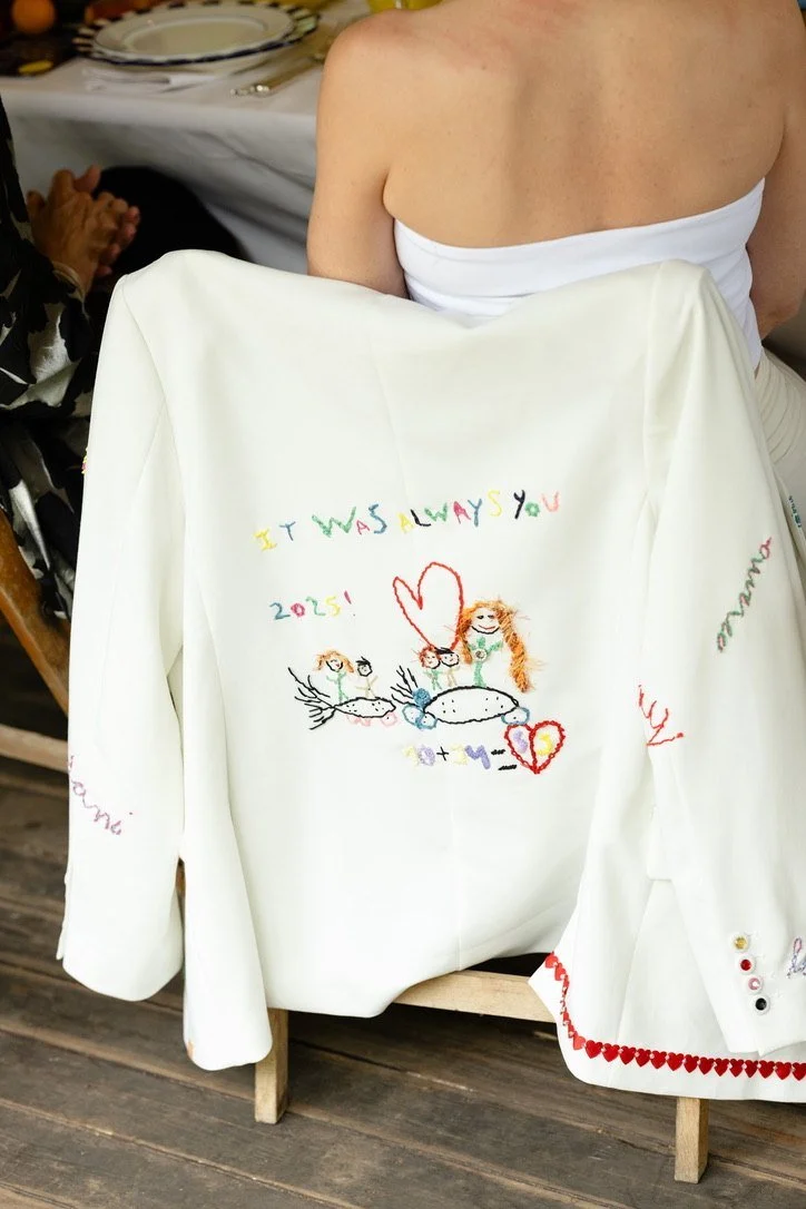 A white blazer embroidered with It was always you and a childlike drawing