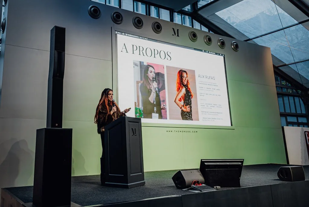 A speaker presenting at a lectern in the glass pavilion
