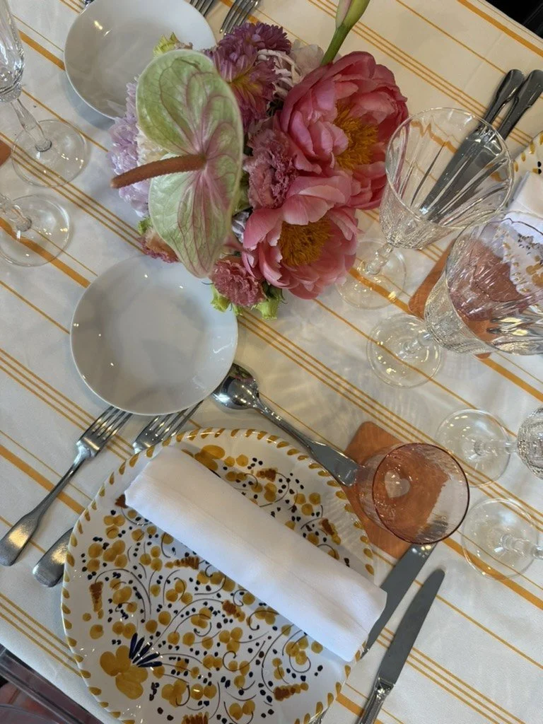 A place setting with a hand-painted plate, rose glass and coral peonies on striped linen