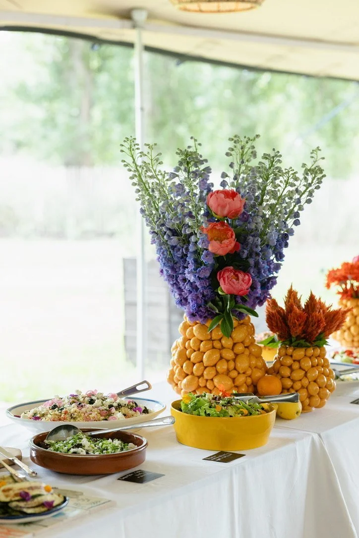 A buffet with delphinium and peonies in a pineapple-shaped vase