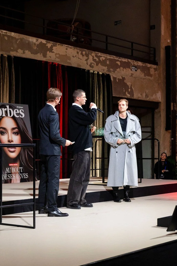 A winner receiving an award on stage next to the Forbes cover