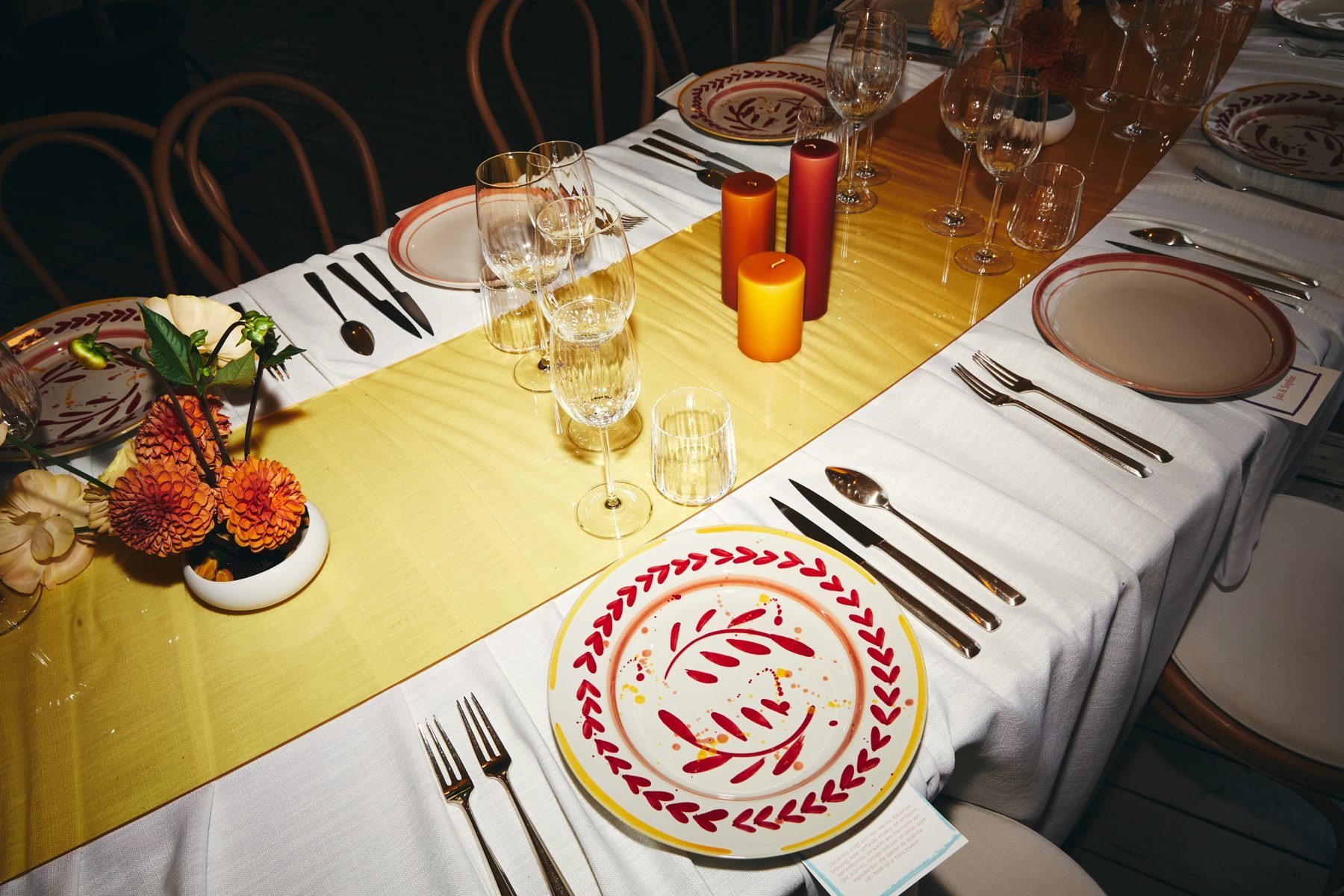 A long table under a yellow tent with ochre runner, patterned plates and orange glassware