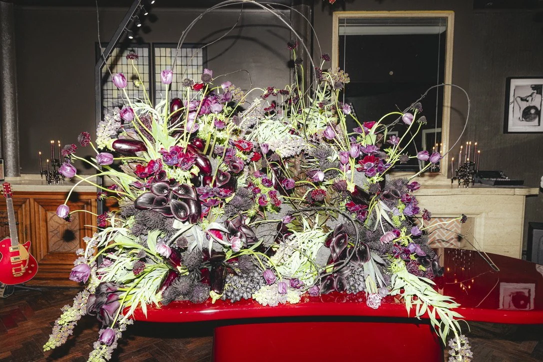 A large arrangement of dark tulips, calla lilies and thistles on a red piano