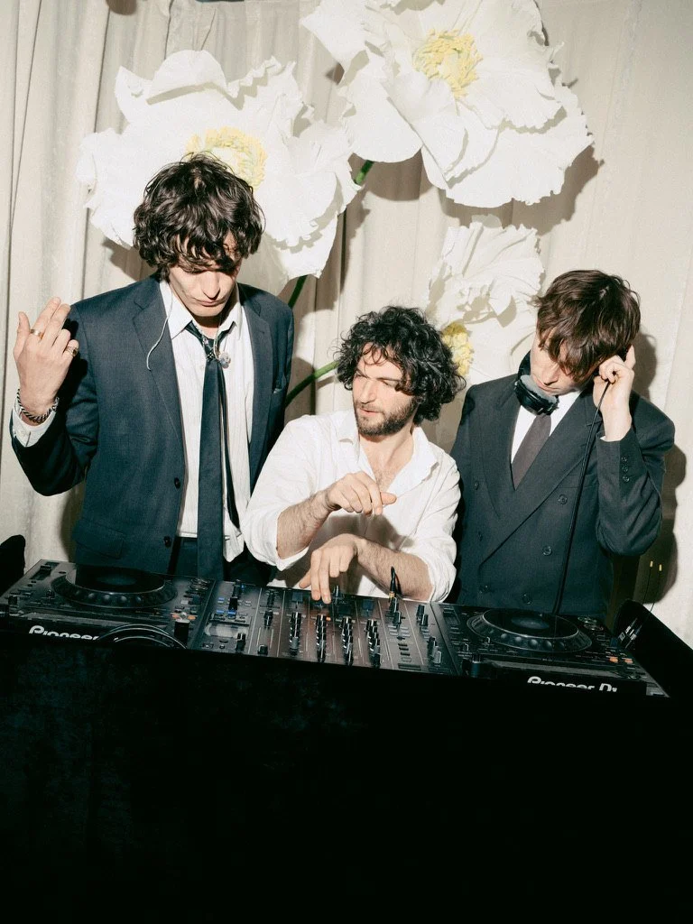 Three DJs in front of giant white paper flowers