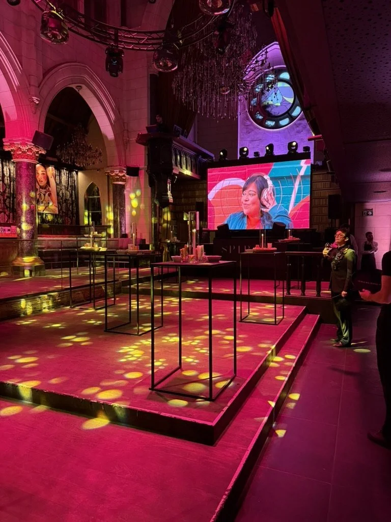 The venue before doors open: arches, chandeliers and cocktail tables in pink light