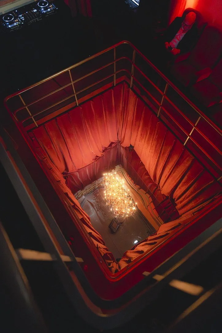 A crystal chandelier glowing at the bottom of a red velvet stairwell