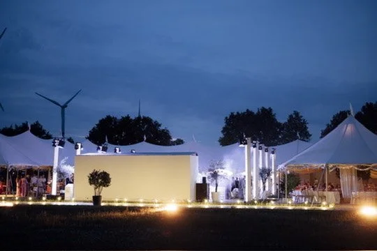 The sailcloth tents lit up at blue hour, wind turbines behind