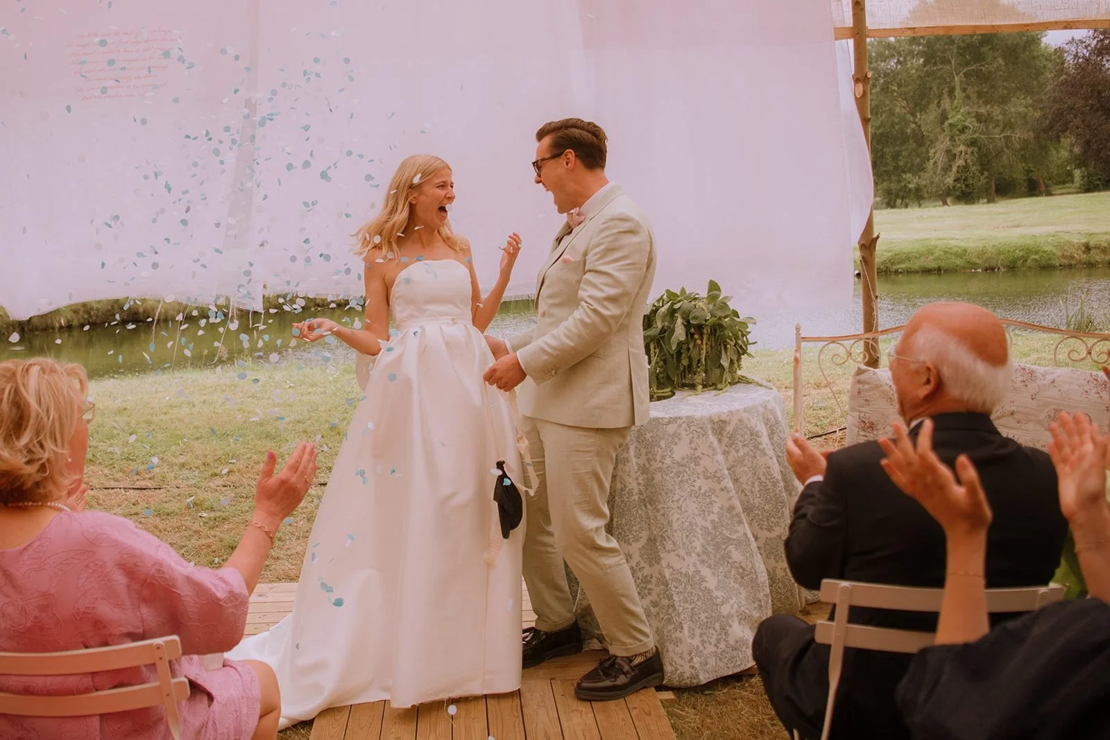 The couple laughing under falling confetti during the ceremony