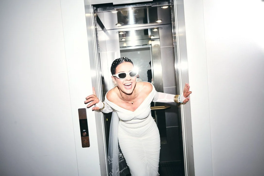 The bride laughing as she steps out of a lift in sunglasses