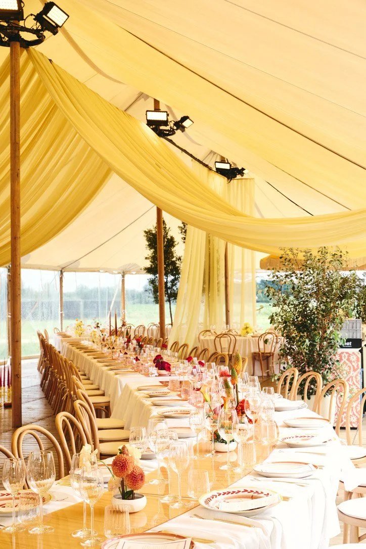 A long wedding table under draped yellow tent fabric
