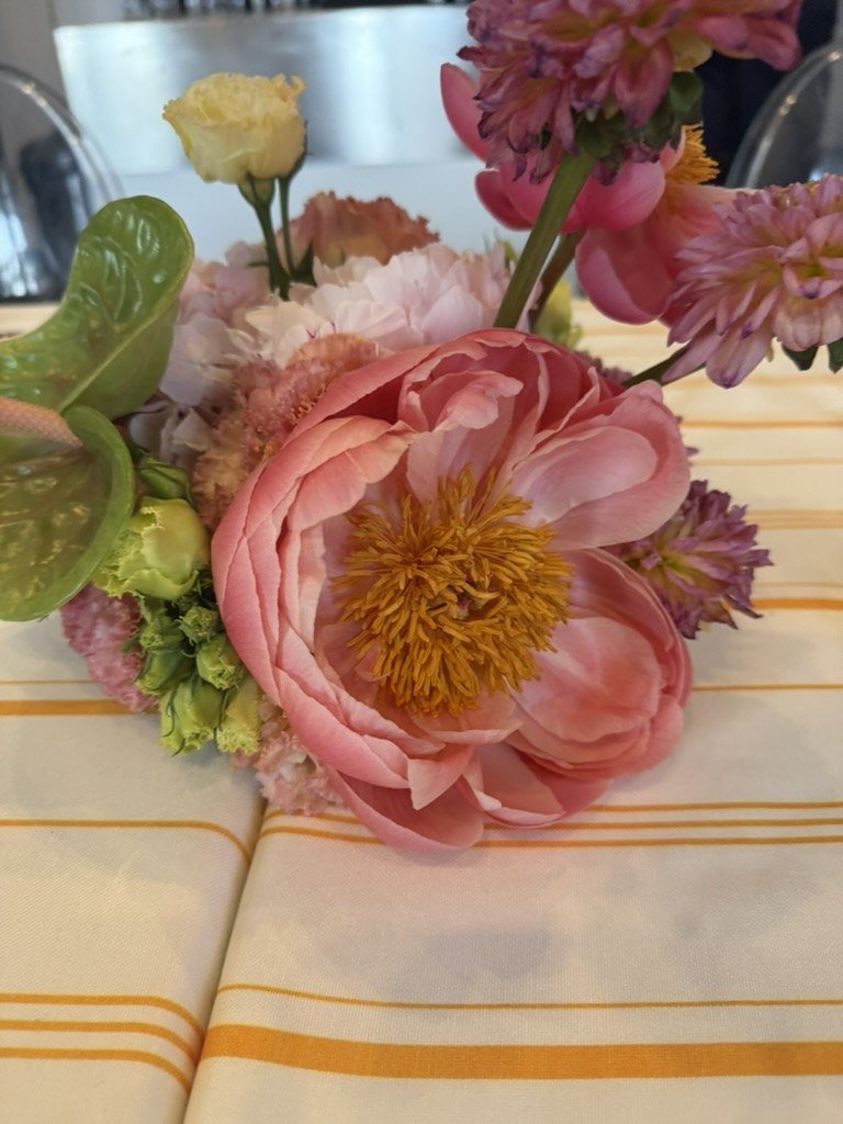 A coral peony arrangement with dahlias and anthurium on striped linen