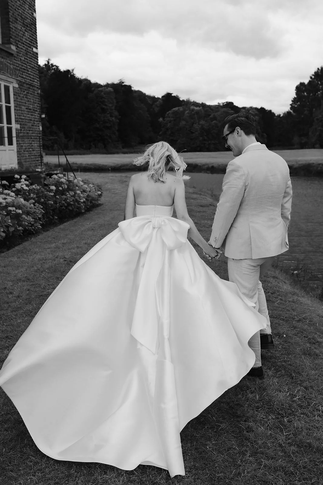 Black-and-white photo of a bride with a large bow walking hand in hand with the groom