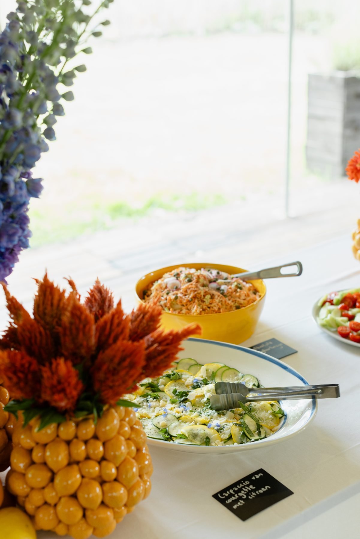 A harvest table with a pineapple, flowers and colourful salads