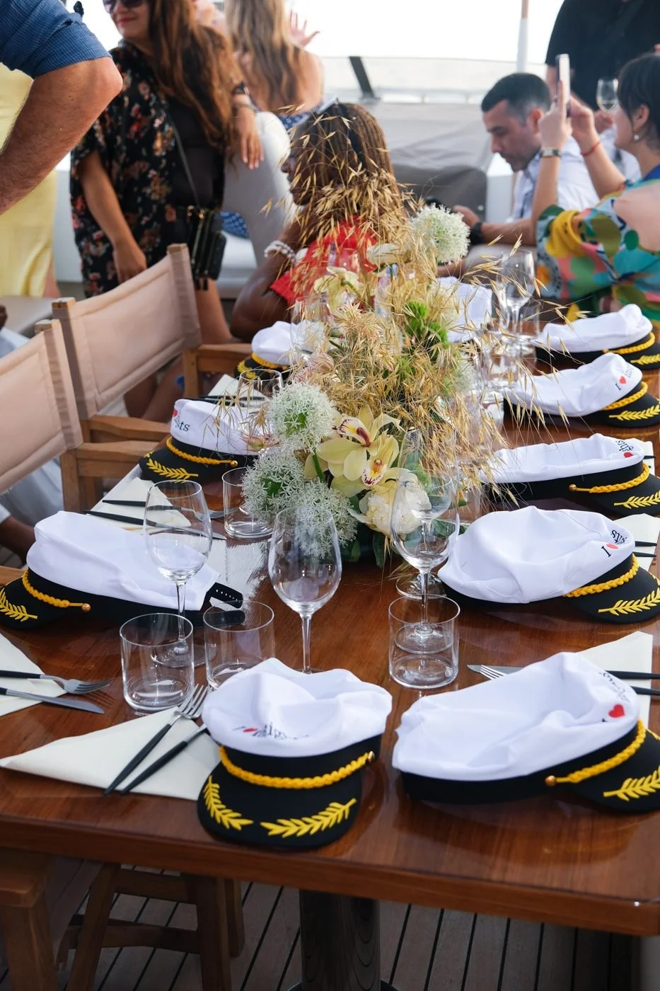 A long table set for dinner on deck with flowers and white napkins