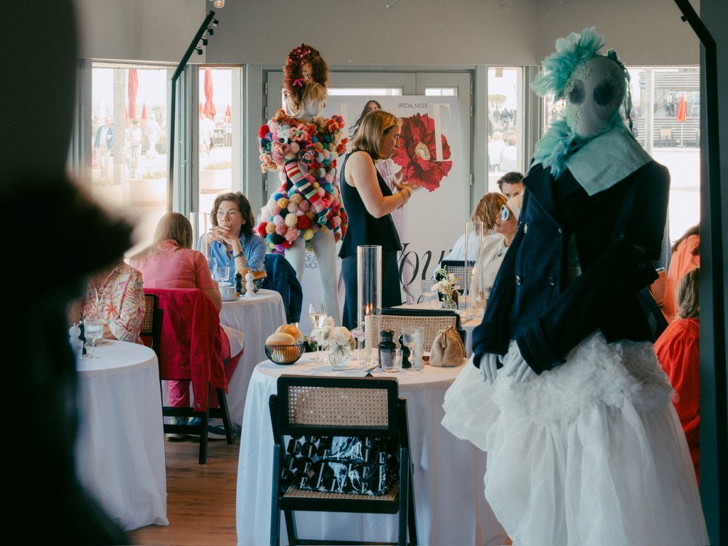 Lunch guests at round tables between couture mannequins, the seafront behind