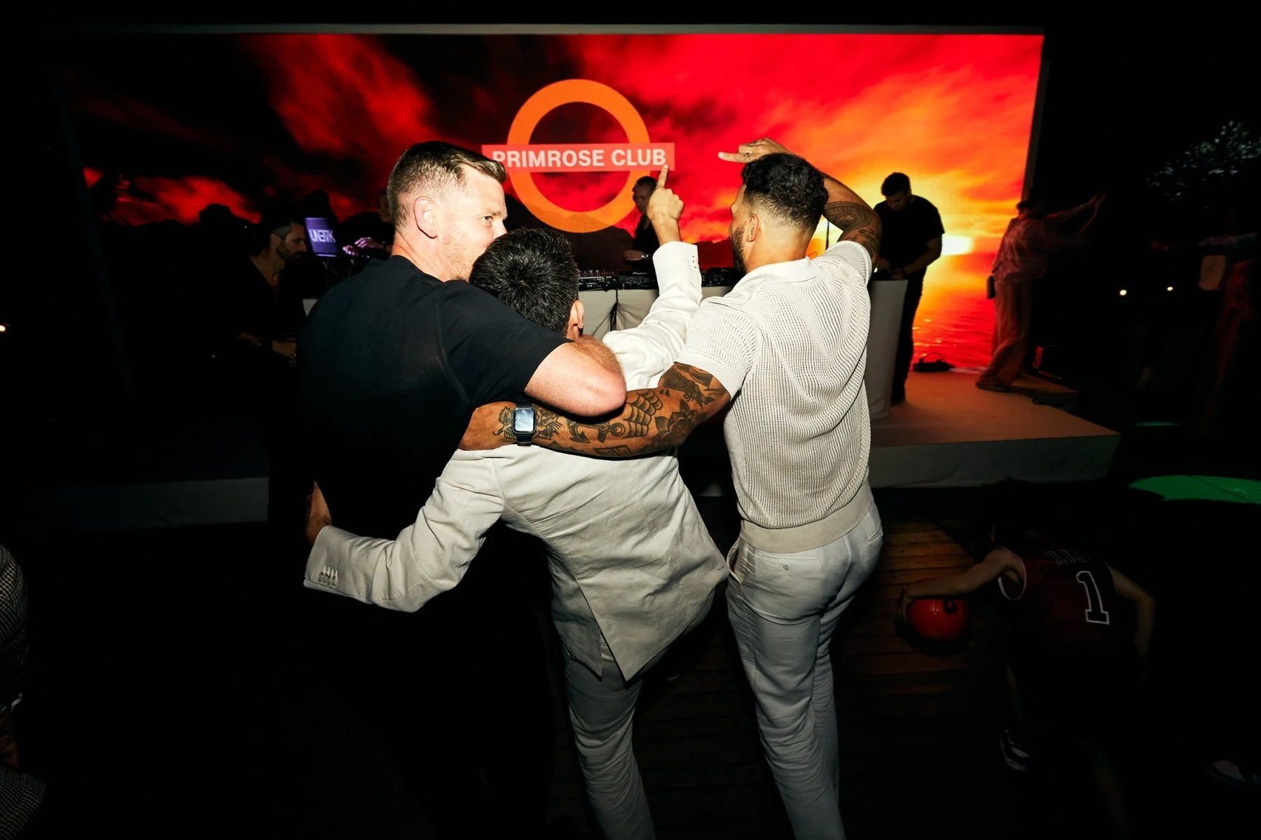 Friends dancing arm in arm in front of the Primrose Club screen and DJ booth