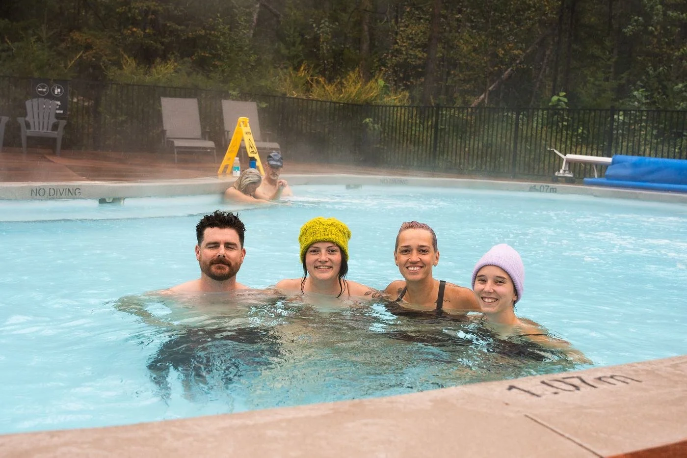 Four friends in colourful toques soaking together in a steaming pool in the fall