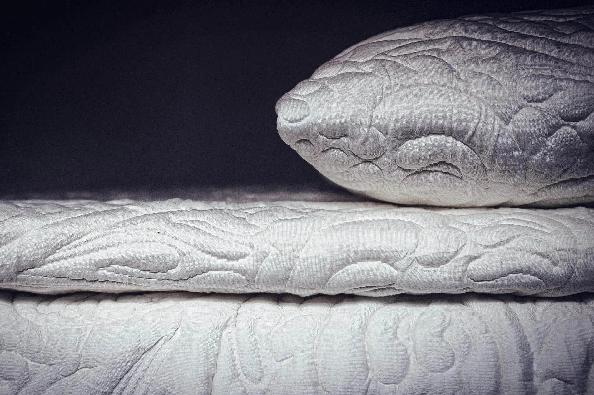 Close-up of the quilted stitching on a white Posh+Lavish mattress cover and pillow