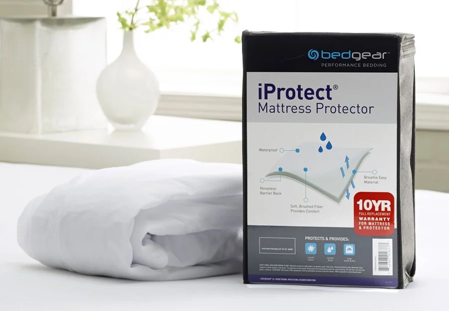 Bedgear iProtect Mattress Protector in its white and grey package, beside the folded white protector on a bed
