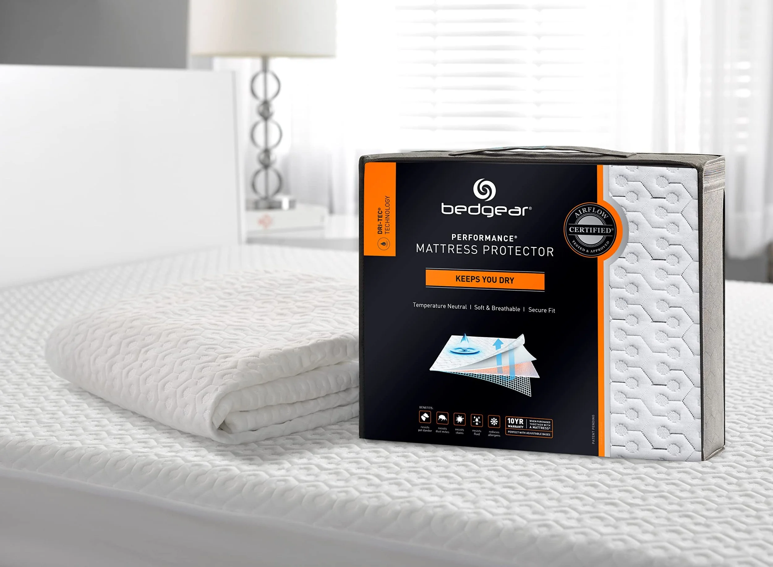 Bedgear Dri-Tec Mattress Protector in its black package with an orange Keeps You Dry band, beside the folded protector on a bed