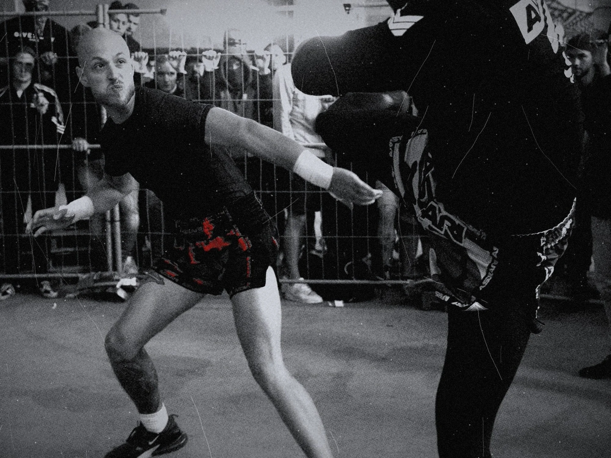 A fighter leaning away from a high kick, masked crowd at the fence