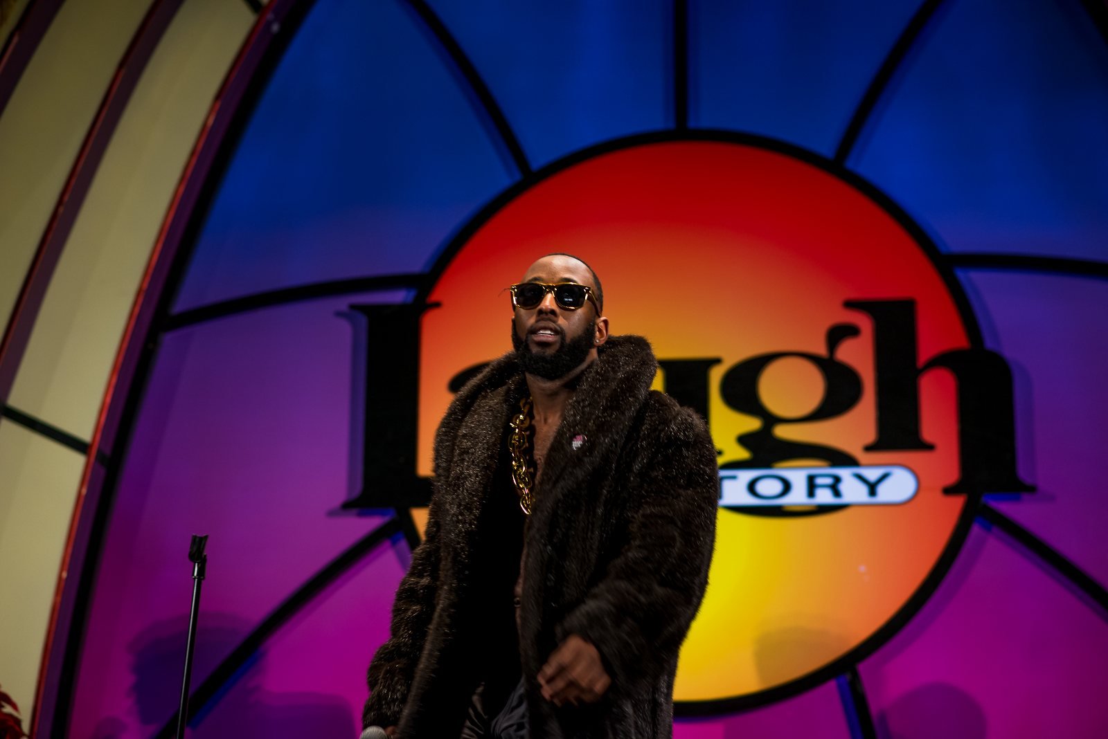 St. James Jackson wearing sunglasses and a fur coat on the Laugh Factory stage.