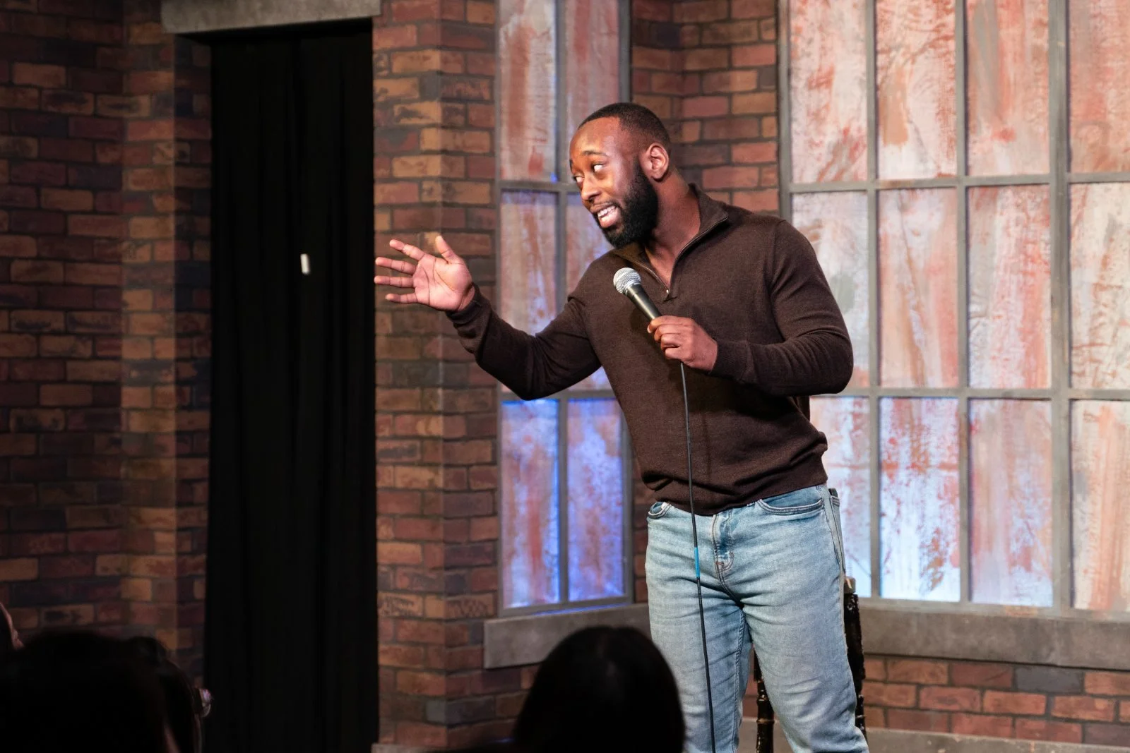 St. James Jackson gesturing with a microphone on a stage with a brick backdrop.