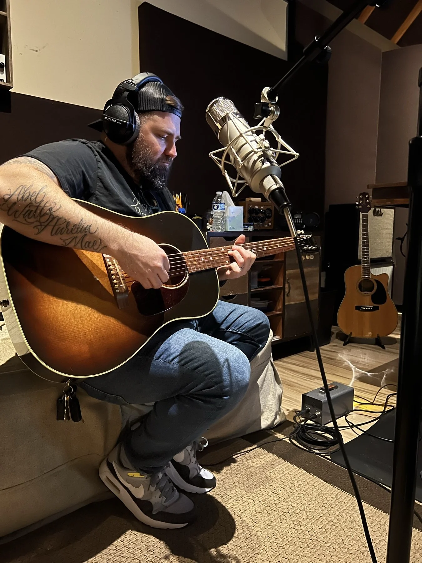 An artist playing acoustic guitar and singing into a studio microphone