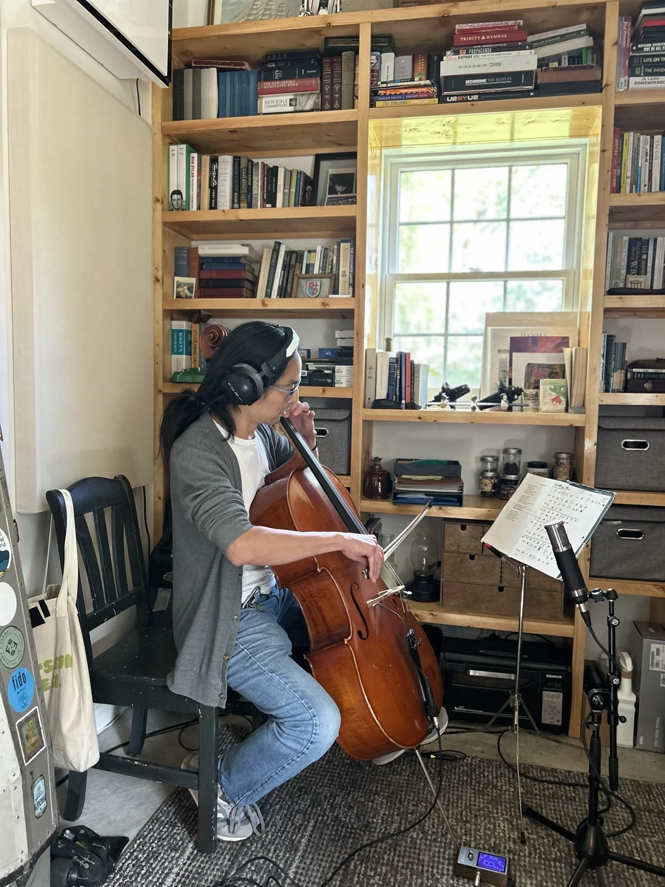 A cellist recording in a room with headphones and a music stand