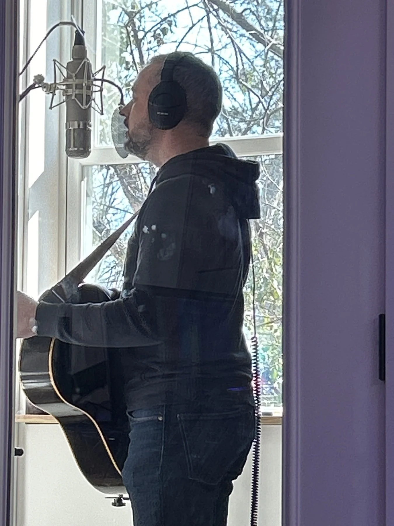 An artist singing and playing acoustic guitar beside a studio microphone