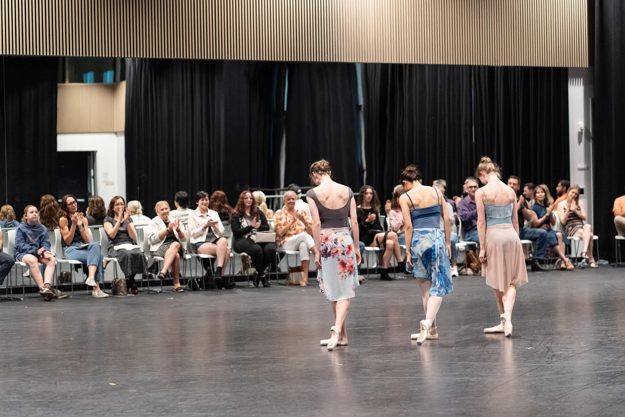 Dancers bow to an audience seated beside the studio floor at an open rehearsal.