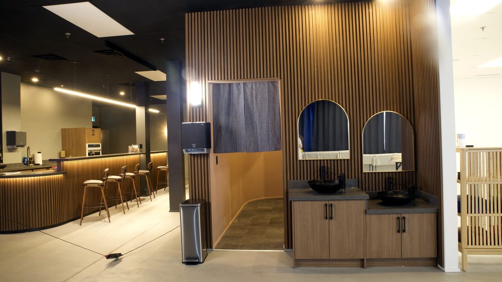 The wash area as built, August 2024: wood slat walls, two arched mirrors and two basins. The photo is the closest built view to the render's angle.