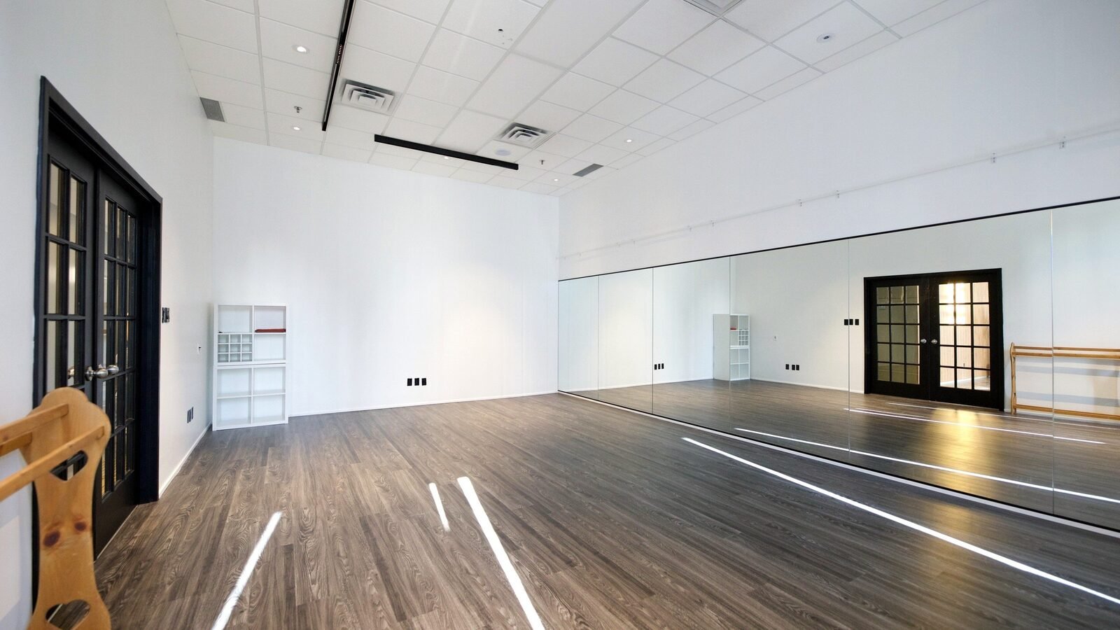 The studio as built, August 2024: a bright room with a wood floor, a mirror wall and black French doors. The photo is the closest built view to the render's angle.