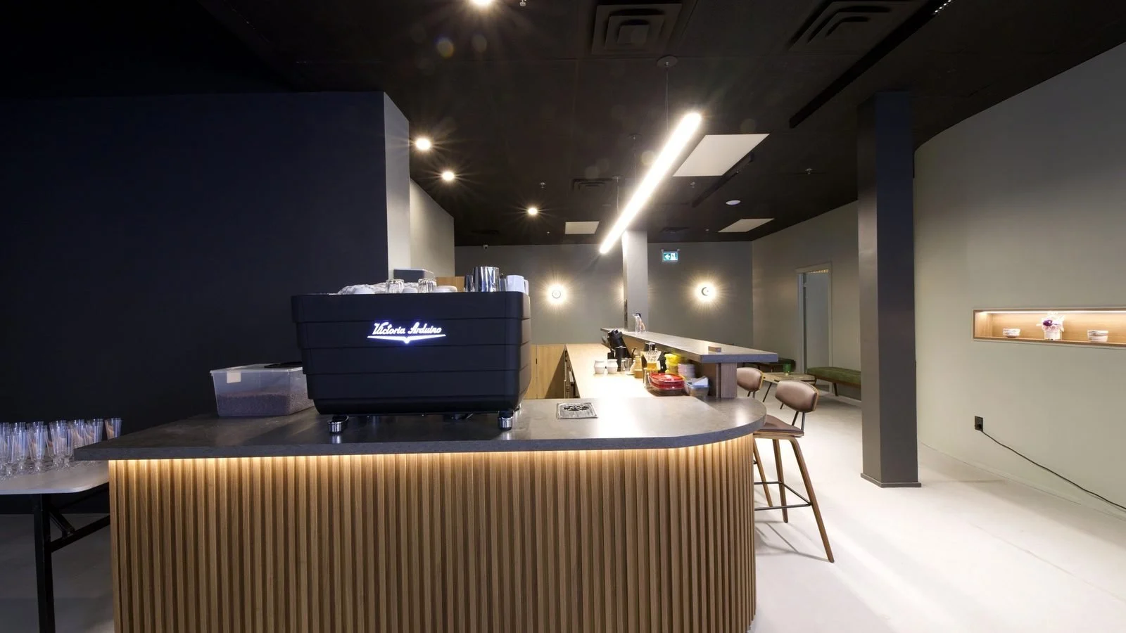 The coffee bar as built, August 2024: the curved wood slat counter with an espresso machine. The photo is the closest built view to the render's angle.