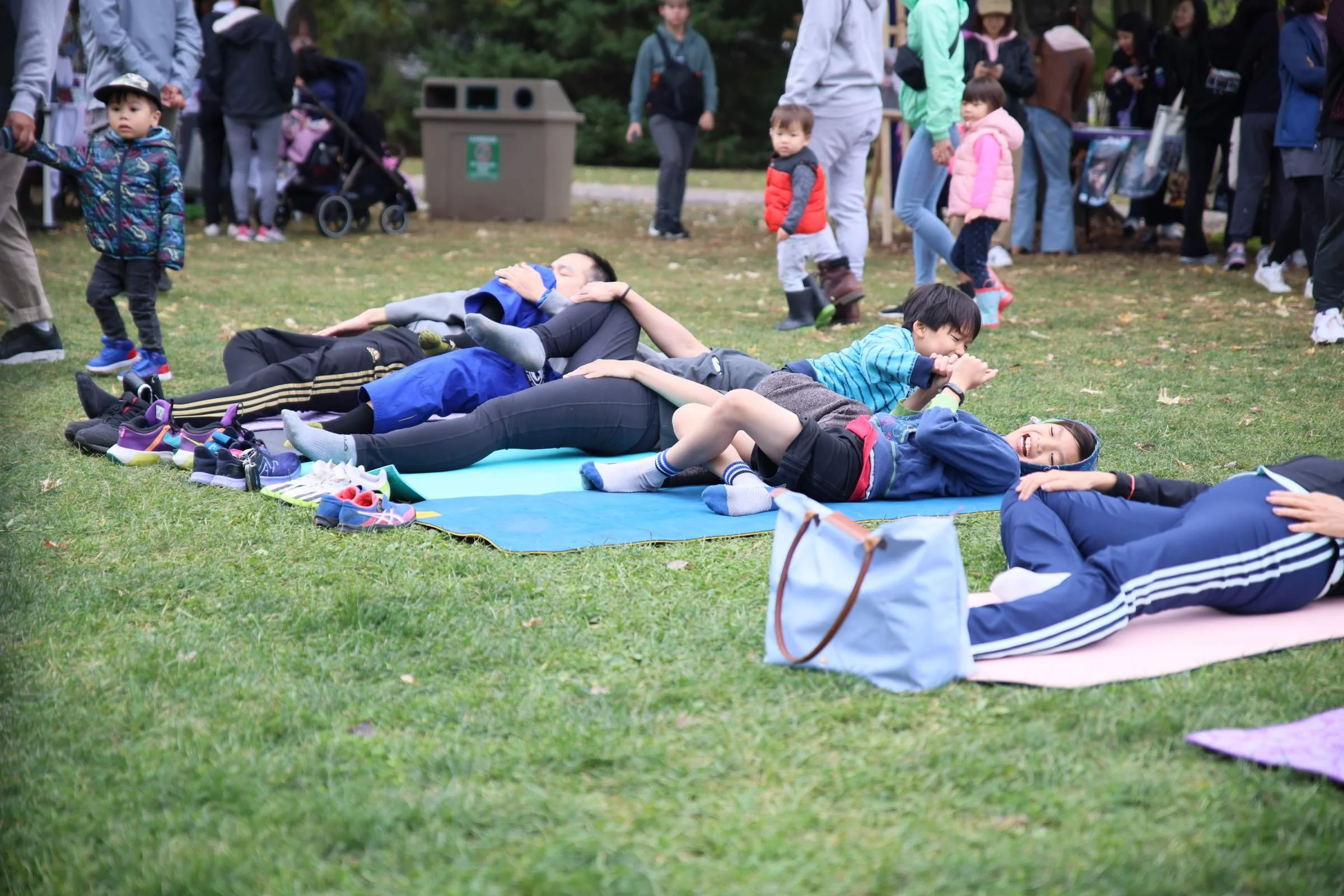 People lie on yoga mats on the museum lawn while visitors walk past behind them.