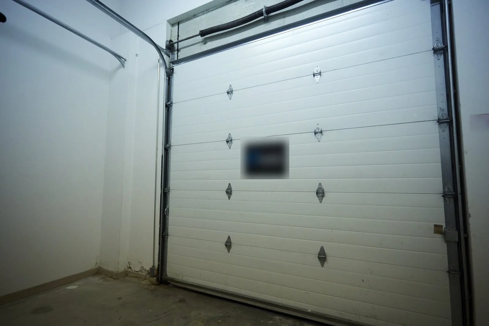 Before, March 2024: a close view of the garage door in the empty hall. A sticker is blurred.