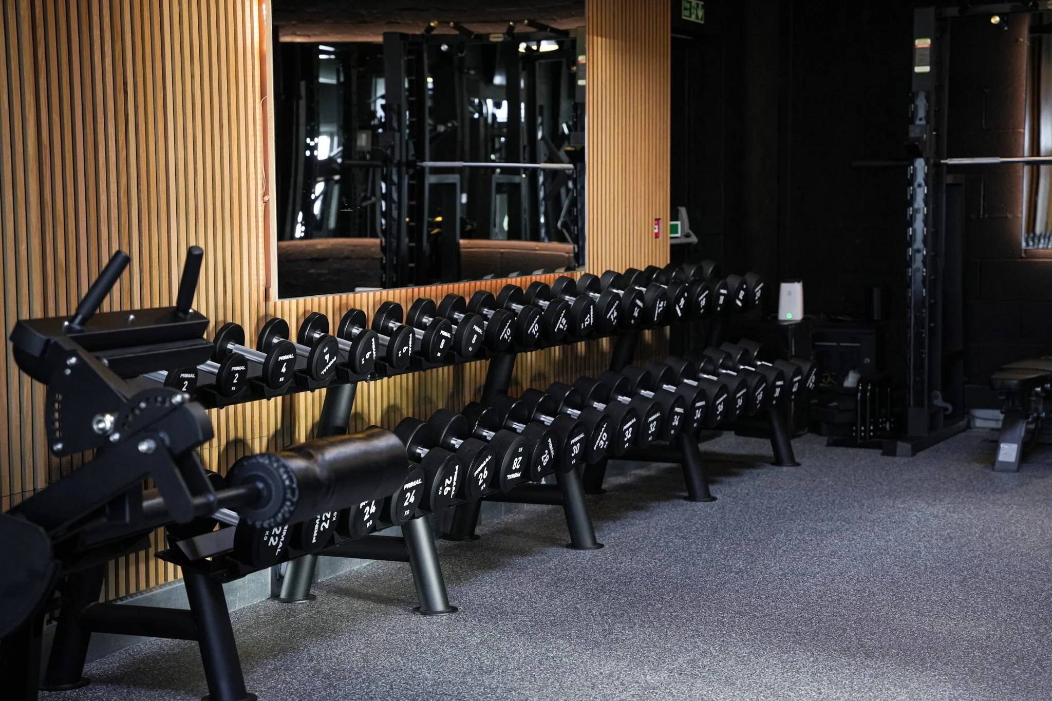 Rows of dumbbells on racks against the copper slat wall at Physique Pro Gosforth, Bakers Yard