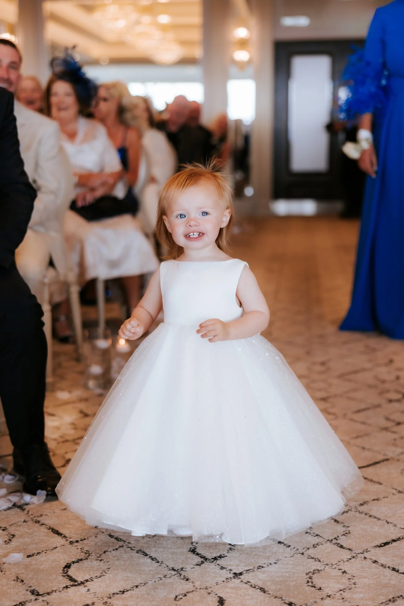 A young flower girl smiling as she walks down the aisle.