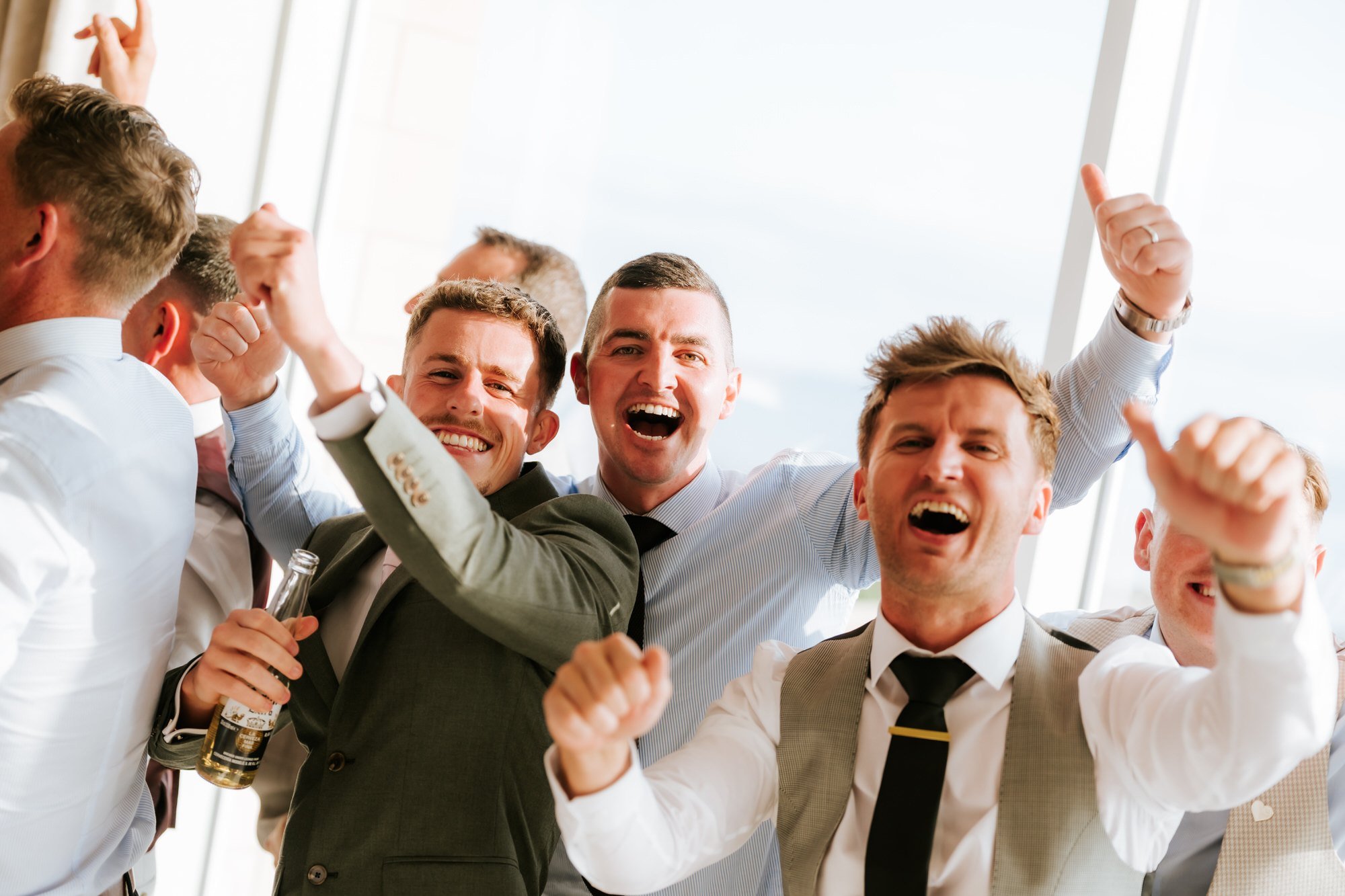 Three wedding guests cheering together with their arms raised.