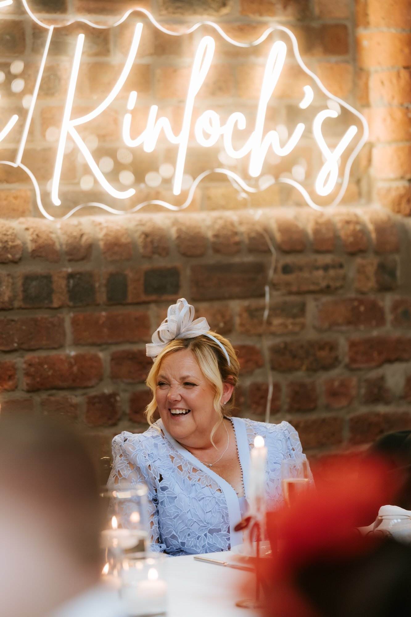 A guest in a pale blue outfit laughing beneath the couple's neon sign.