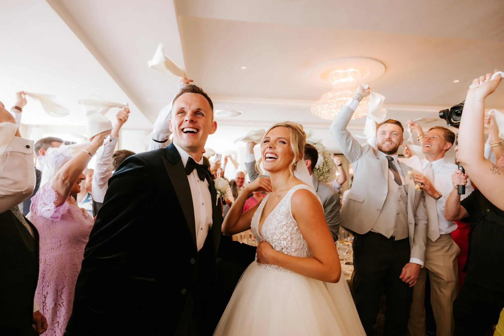 Nicole and Lawrence surrounded by guests waving napkins at the wedding breakfast.