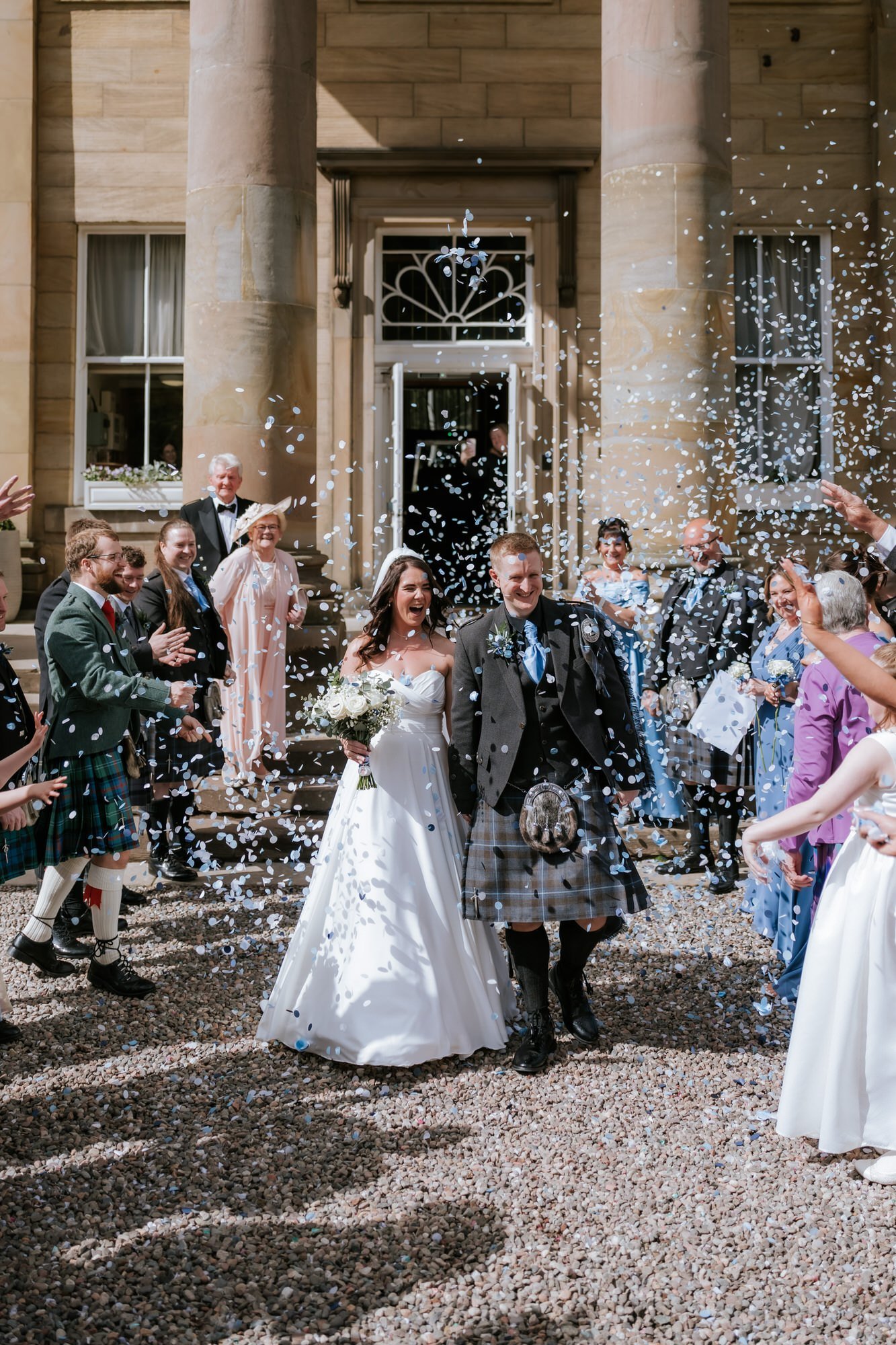 Steph and Calum walking through confetti outside Balbirnie House.