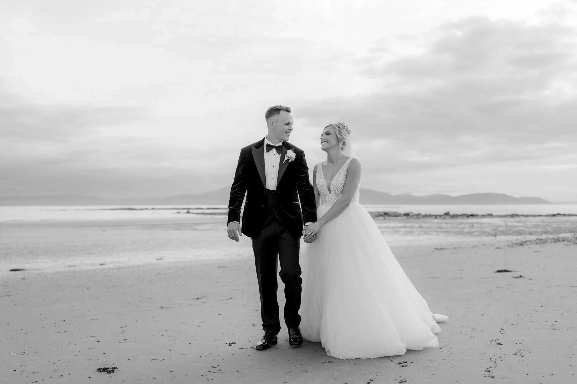 The newlyweds walking hand in hand on the beach in black and white.