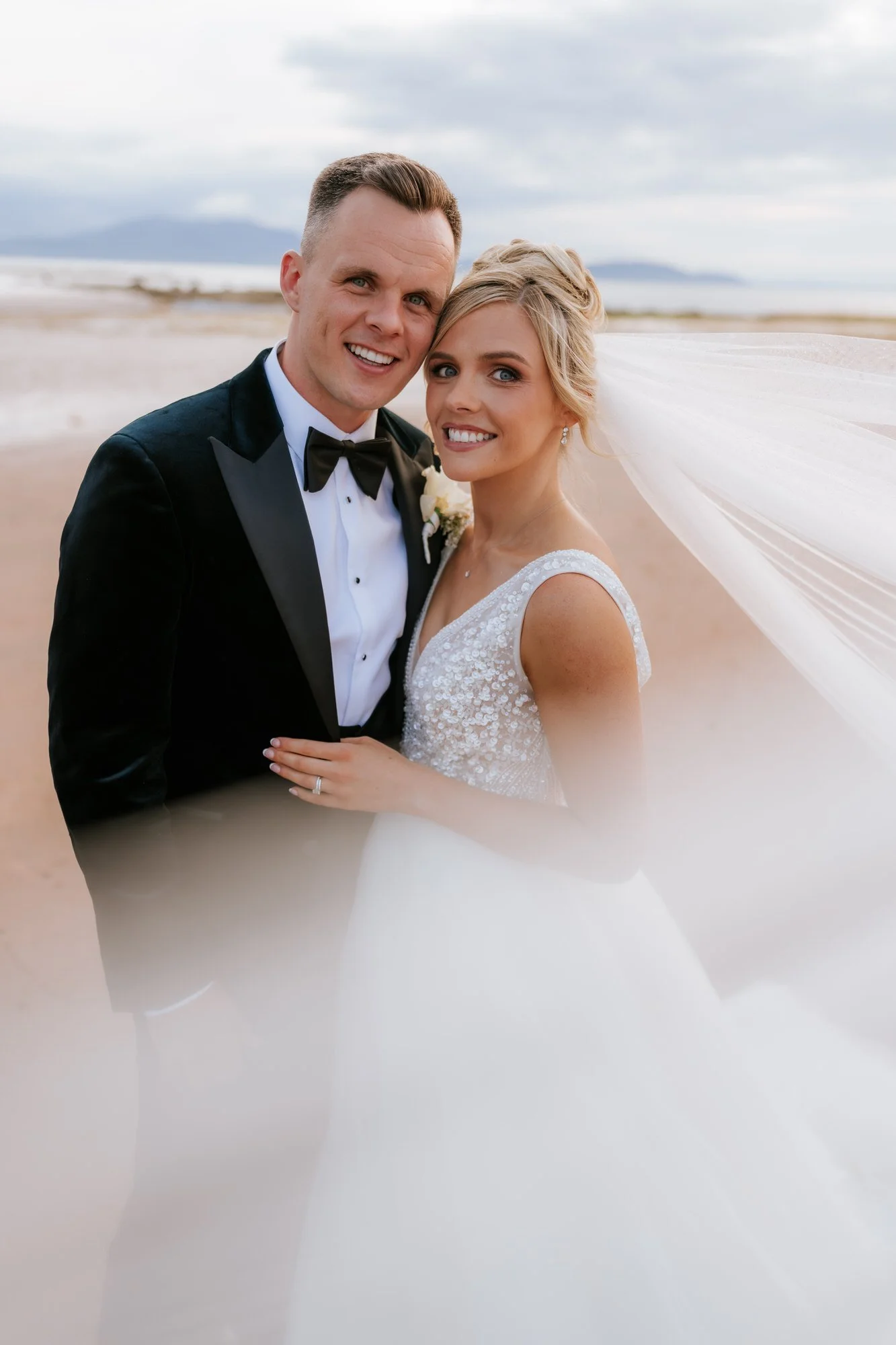 Nicole and Lawrence smiling beneath her veil during their beach portraits.