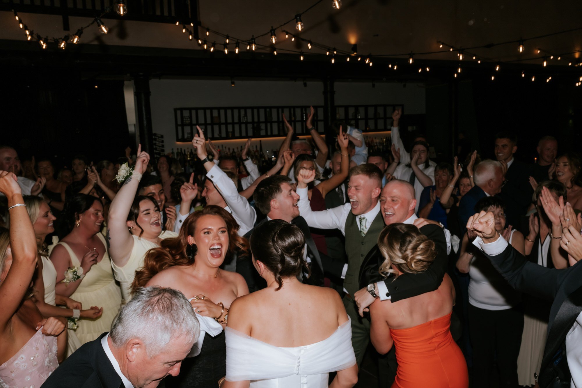 Wedding guests filling the dance floor with their hands in the air.
