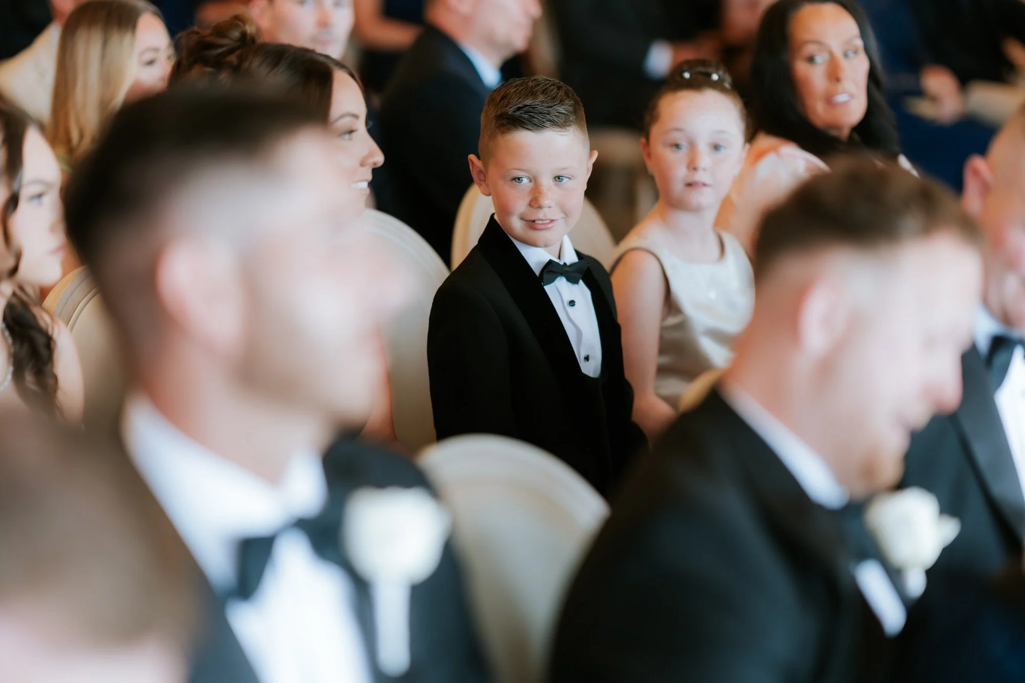 A young guest in a tuxedo watching the wedding ceremony.