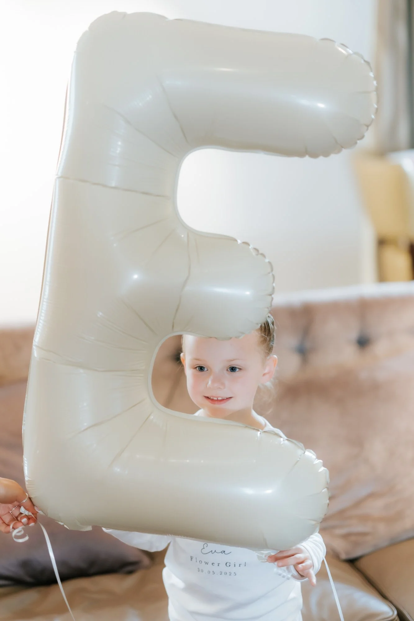 A flower girl peeking through a large letter E balloon during preparations.