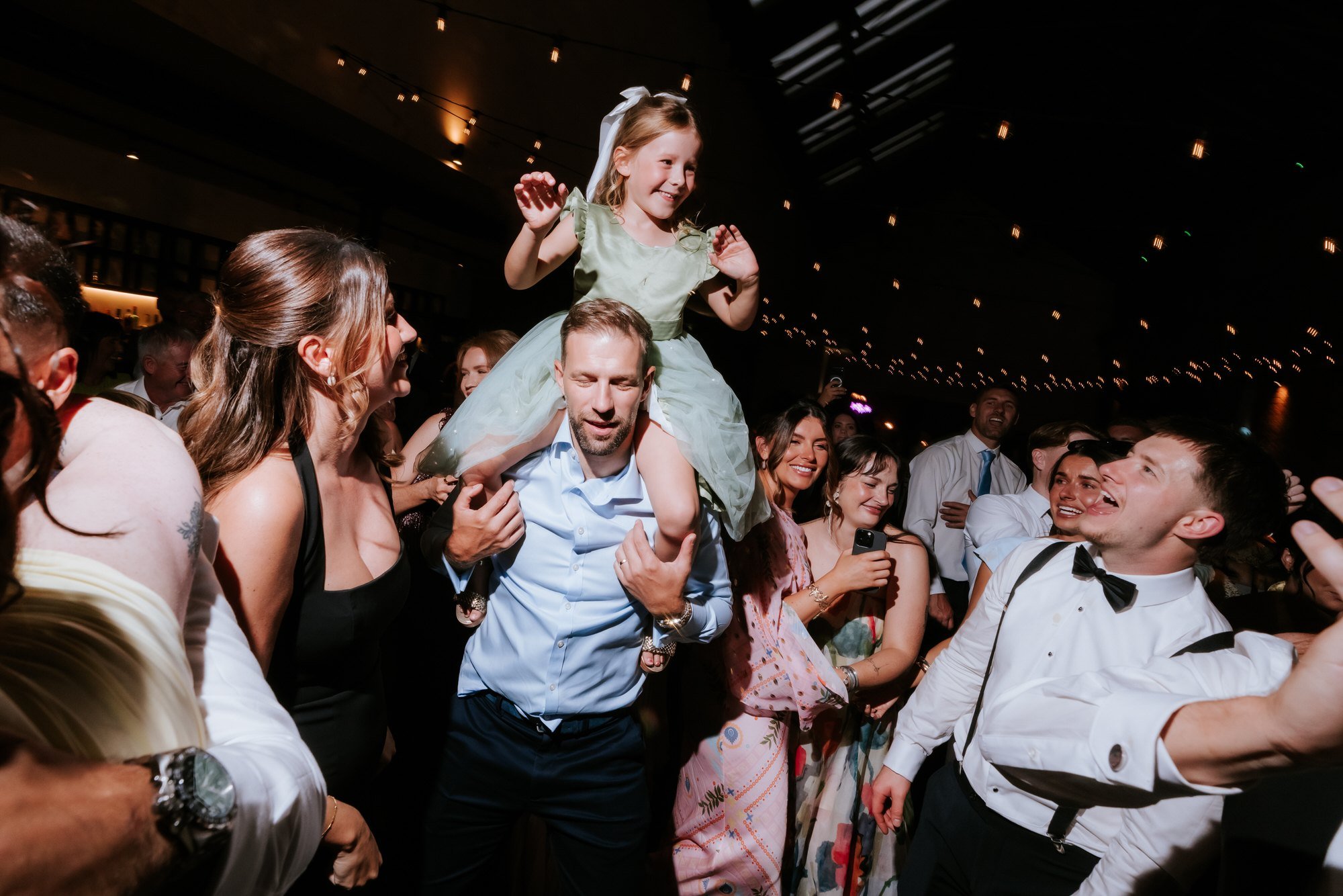 A child dancing on a guest's shoulders in the middle of the wedding party.