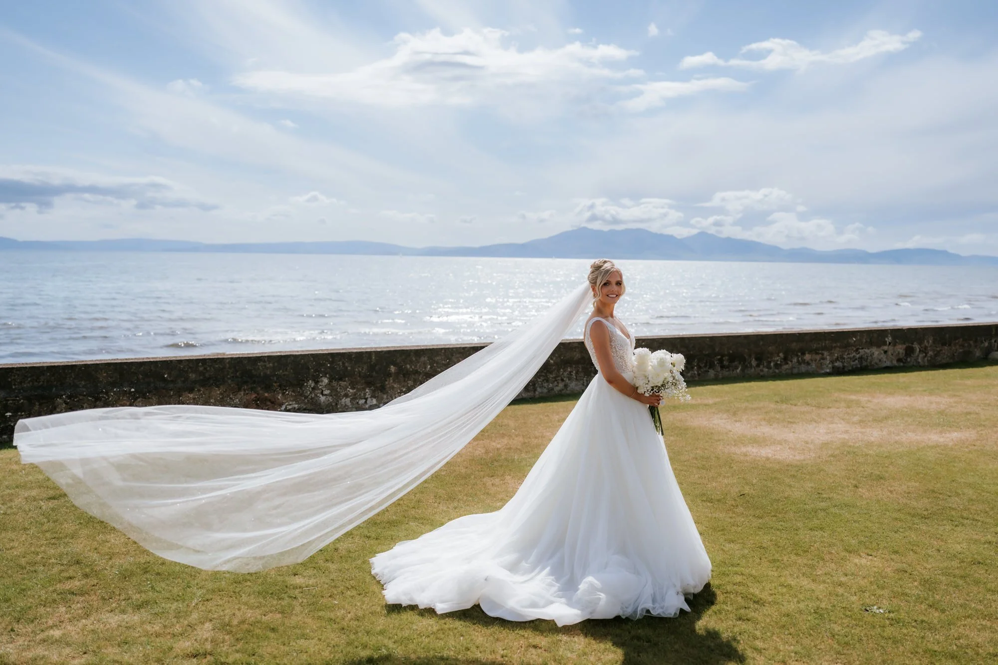 Nicole standing by the coast with her veil catching the breeze.