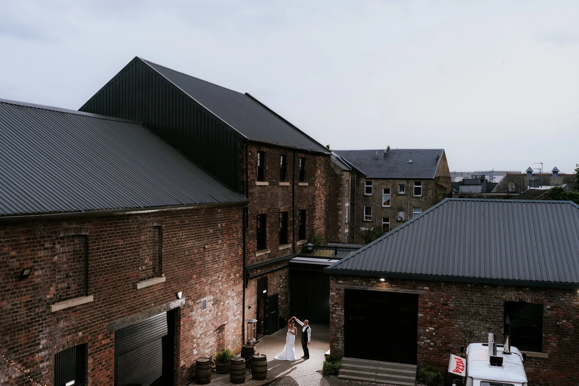 A wide view of the red-brick buildings at The Engine Works with Caitlin and Craig dancing in the courtyard.